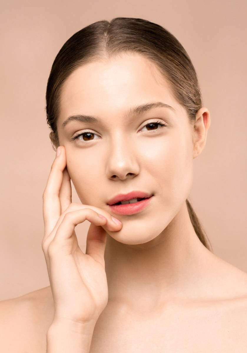 Người mẫu chạm nhẹ lên gò má căng mịn trên nền hồng đào