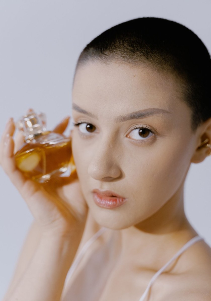 Người mẫu cầm chai nước hoa hổ phách cạnh gương mặt
